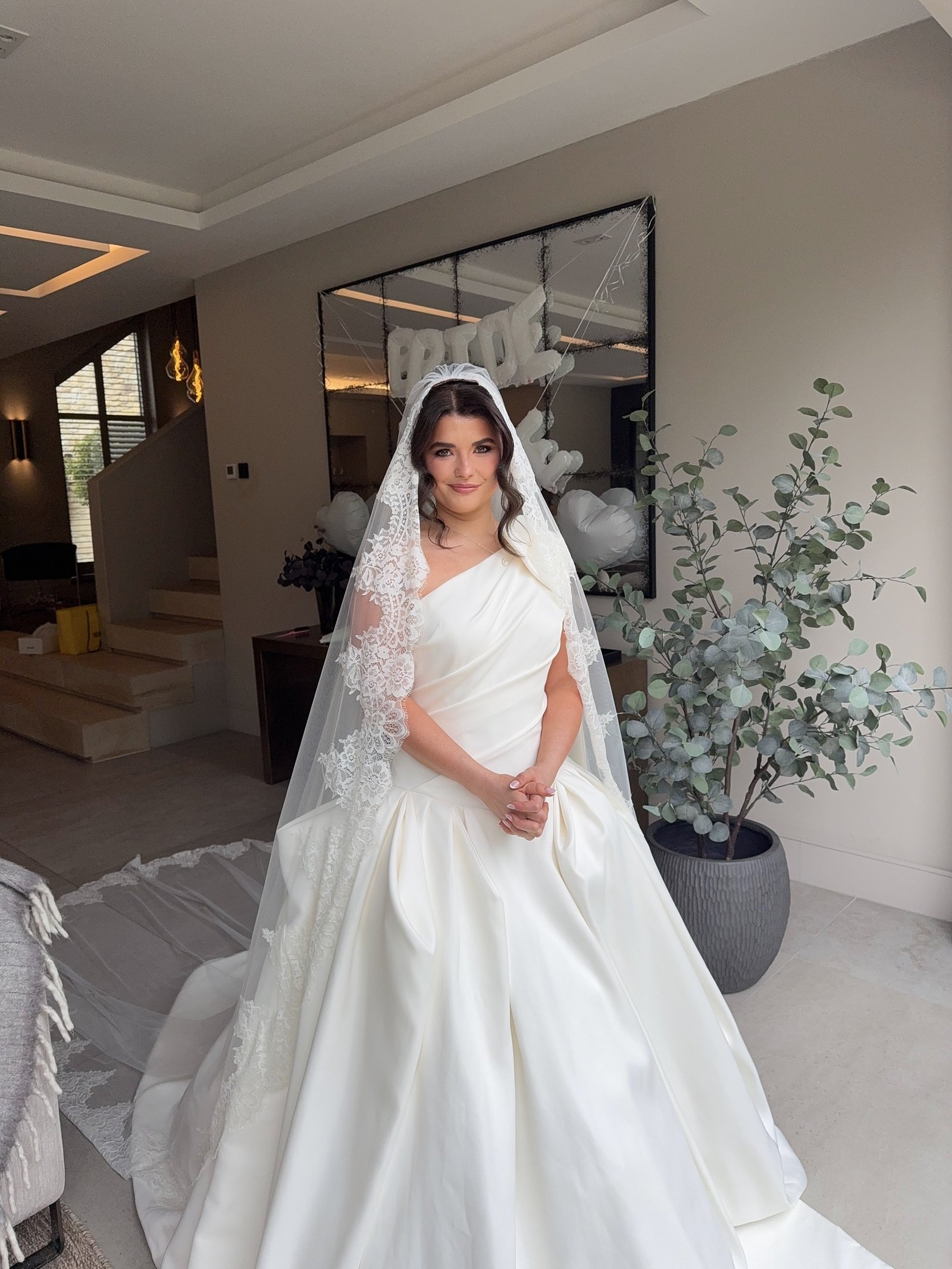 Bride in a lace veil and satin gown with soft, radiant bridal makeup