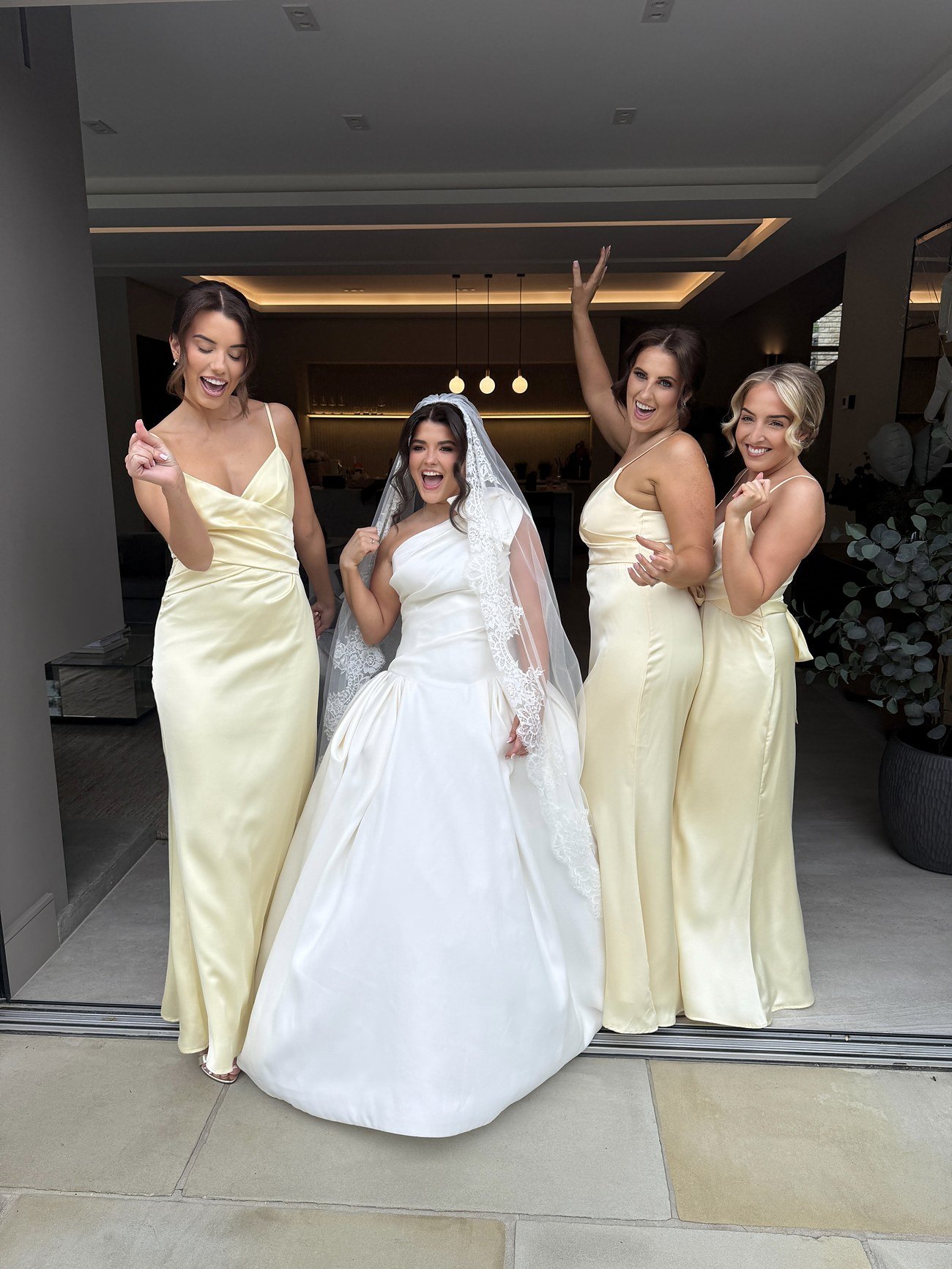Bride and bridesmaids celebrating together in a lace veil and pale yellow satin dresses
