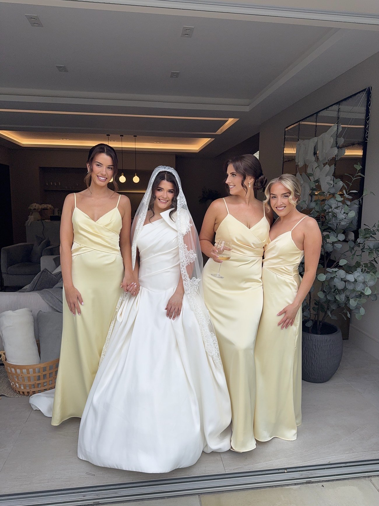 Bride in a veil and ivory gown standing with three bridesmaids in pale yellow dresses