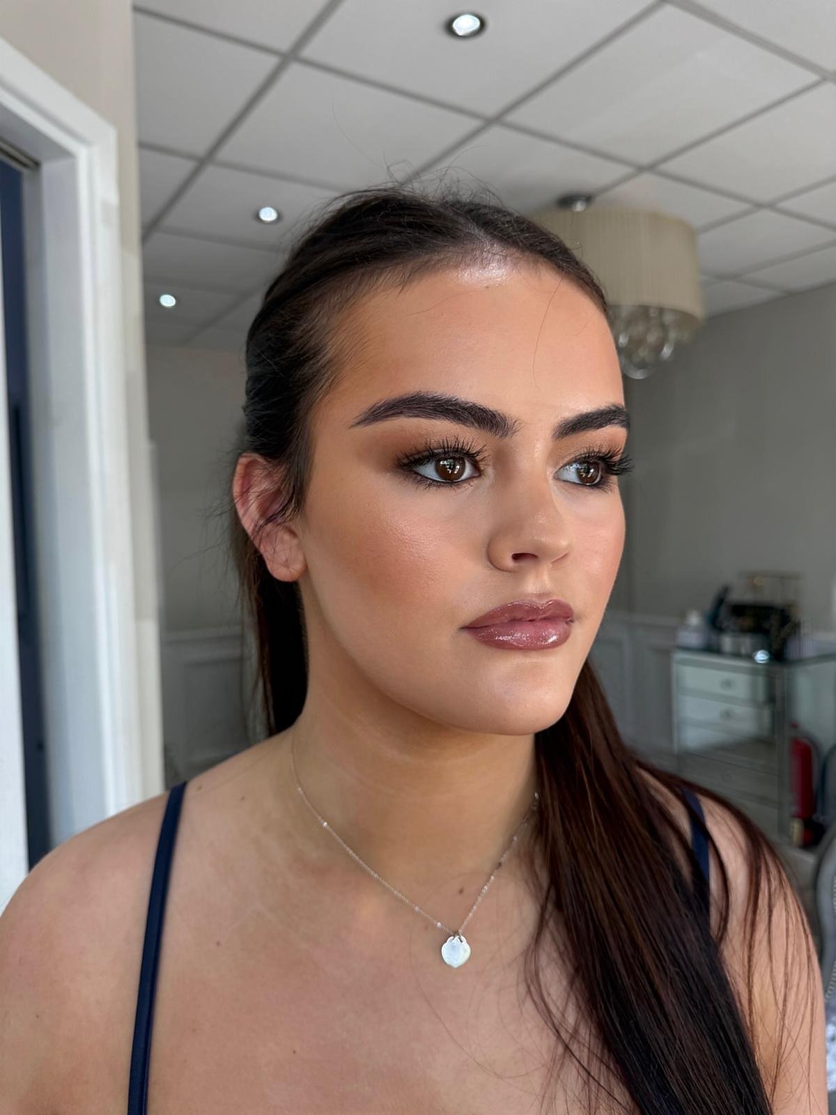 Occasion makeup look: client with dark hair swept back, bold brows, bronze eyes and a glossy mauve lip