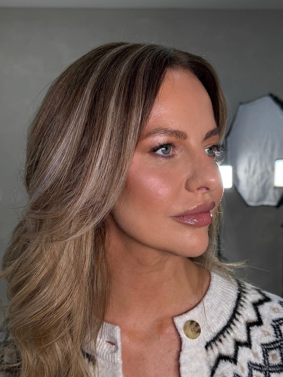 Occasion makeup look: client in profile with soft blonde-brown waves and a glowing, rose-toned finish