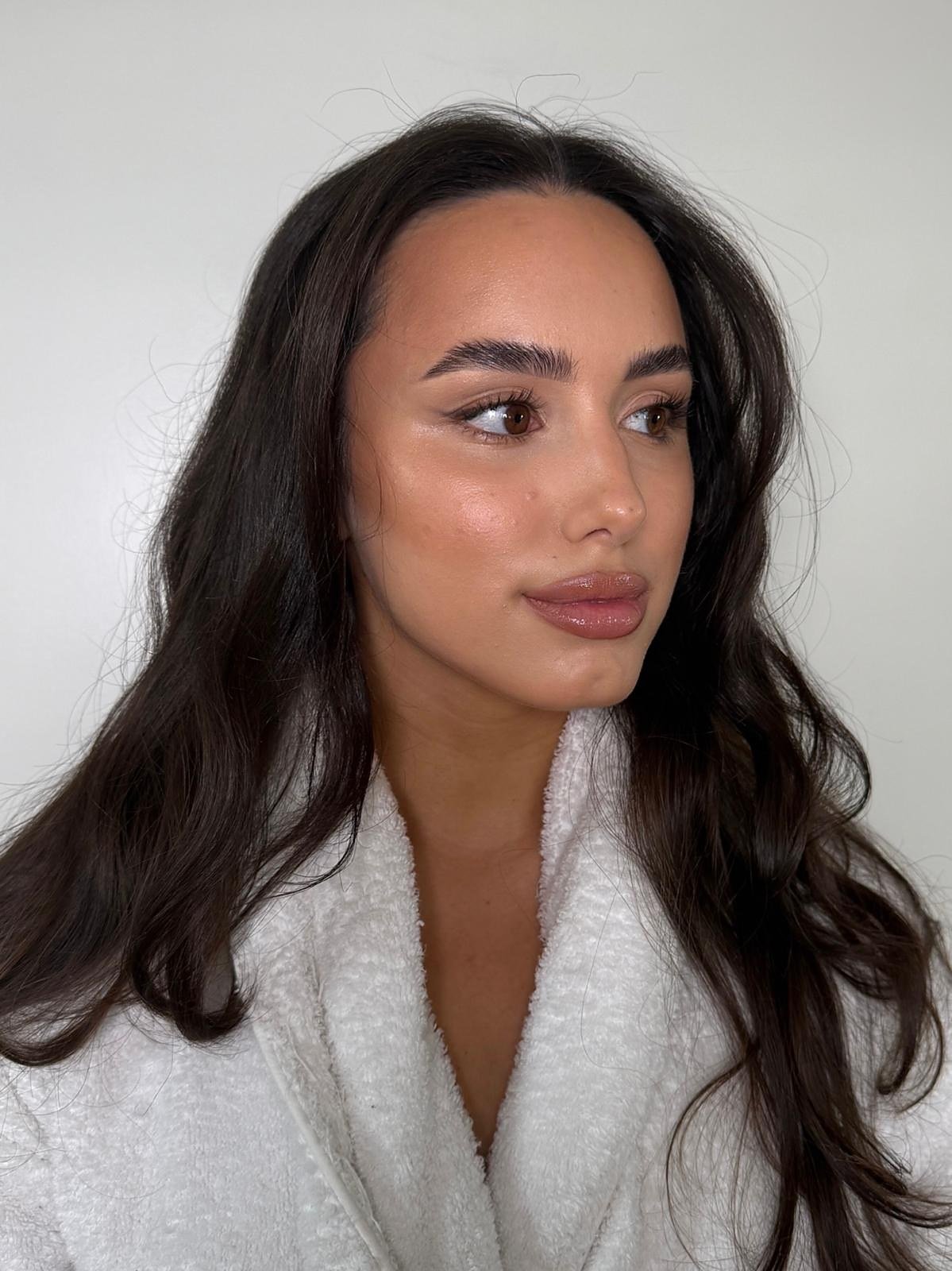 Occasion makeup look: client in a white robe with long dark waves, a luminous complexion and a nude gloss lip